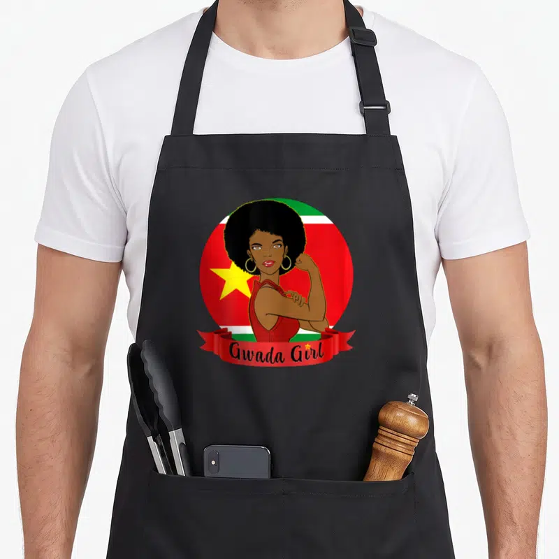 Tablier de cuisine noir avec illustration Gwada Girl et drapeau guadeloupéen en arrière-plan circulaire rouge vert et blanc.