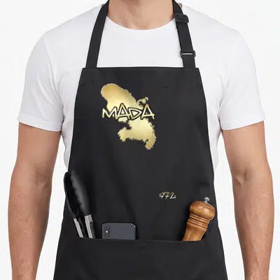 Tablier de cuisine noir avec une carte dorée de la Martinique surmontée du texte MADA et du numéro 972 en bas à droite.