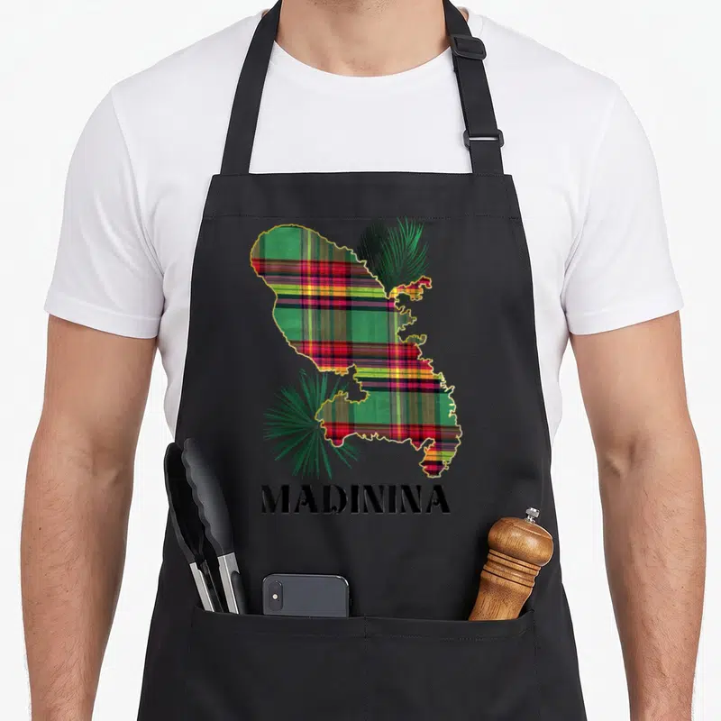 Tablier de cuisine noir avec carte de la Martinique en motif madras et feuilles de palmier vertes.
