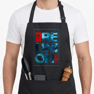 Tablier de cuisine noir avec typographie Réunion 974, vagues bleues et silhouette de palmier rouge encadrée de bleu.