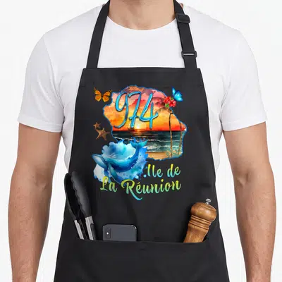 Tablier de cuisine noir avec illustration colorée de la Baleine 974 et d'un coucher de soleil réunionnais.