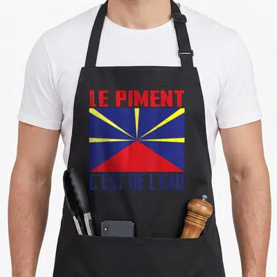 Tablier de cuisine noir avec un motif graphique coloré représentant le drapeau réunionnais et du texte en rouge et bleu.