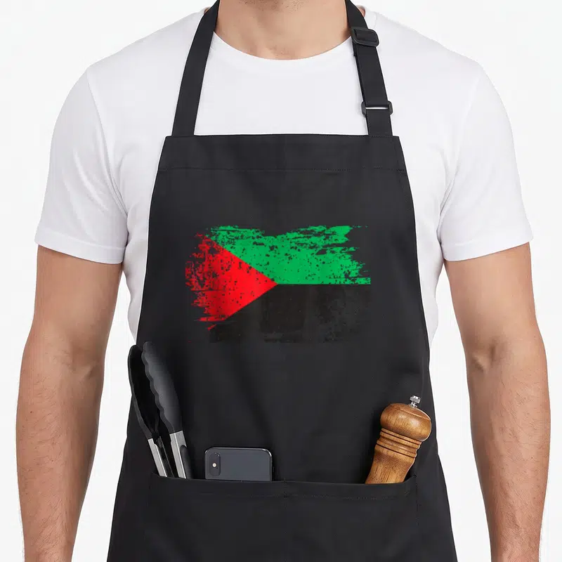 Tablier de cuisine noir avec un drapeau stylisé aux teintes rouges, vertes et noires en aspect vieilli.