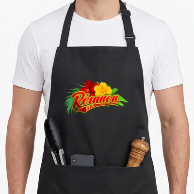 Tablier de cuisine noir avec inscription Réunion 974 Ocean Indien et fleurs d'hibiscus colorées sur fond gris uni.