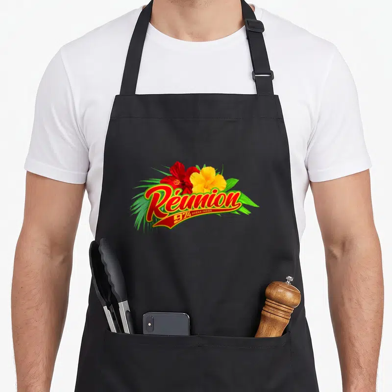 Tablier de cuisine noir avec inscription Réunion 974 Ocean Indien et fleurs d'hibiscus colorées sur fond gris uni.