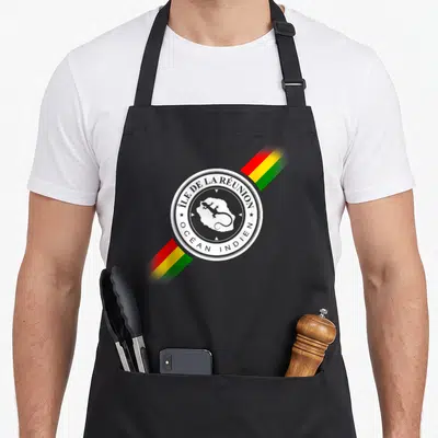Tablier de cuisine noir avec logo circulaire Île de la Réunion et bandes Rasta diagonales.