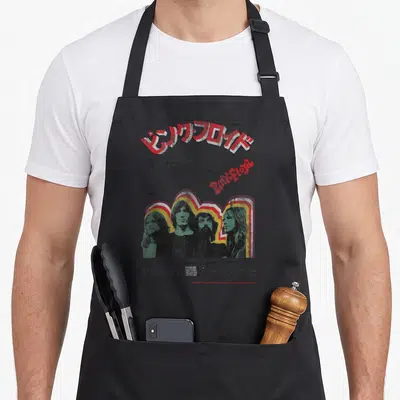 Tablier de cuisine noir avec affiche Pink Floyd Tokyo 1972 et portraits du groupe sur fond gris uni.