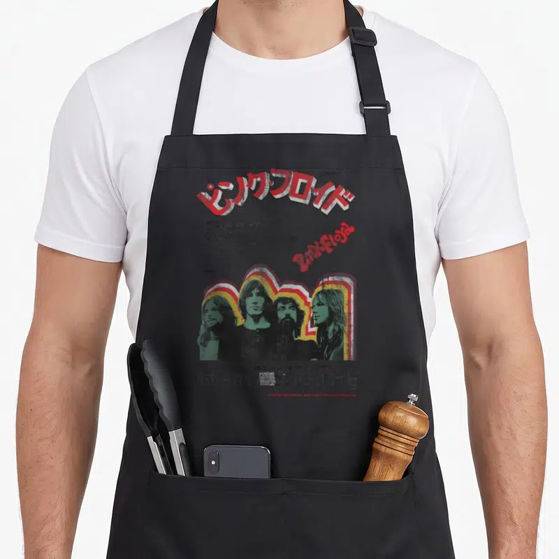 Tablier de cuisine noir avec affiche Pink Floyd Tokyo 1972 et portraits du groupe sur fond gris uni.