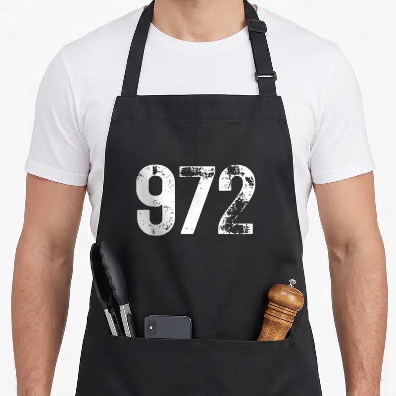 Tablier de cuisine noir avec le code régional 972 Dallas Texas en grandes lettres blanches texturées.