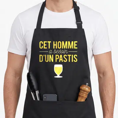 Tablier de cuisine noir avec illustration verre de pastis jaune et texte Cet homme a besoin d'un pastis en lettres capitales jaunes.