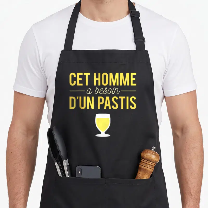 Tablier de cuisine noir avec illustration verre de pastis jaune et texte Cet homme a besoin d'un pastis en lettres capitales jaunes.