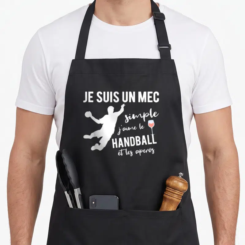 Tablier de cuisine noir avec silhouette blanche de joueur de handball et verre à vin rose, texte blanc centré.