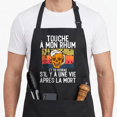 Tablier de cuisine noir avec un crâne tenant une bière et le texte humoristique sur fond rétro.