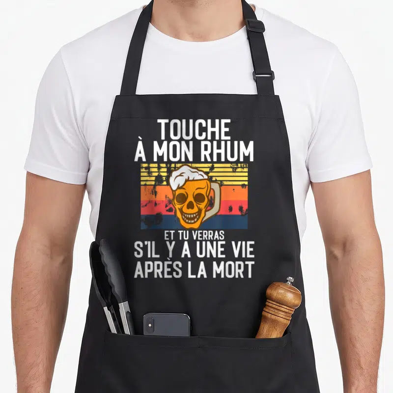 Tablier de cuisine noir avec un crâne tenant une bière et le texte humoristique sur fond rétro.