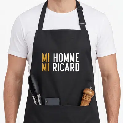 Tablier de cuisine noir avec l'inscription MI HOMME MI RICARD en lettres orange et blanches au centre du torse.