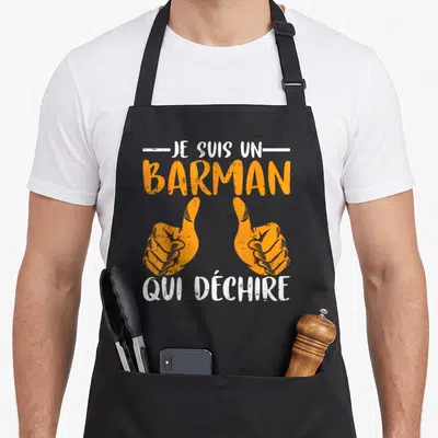 Tablier de cuisine noir avec texte Je Suis Un Barman Qui Déchire et deux mains orange faisant un signe positif.