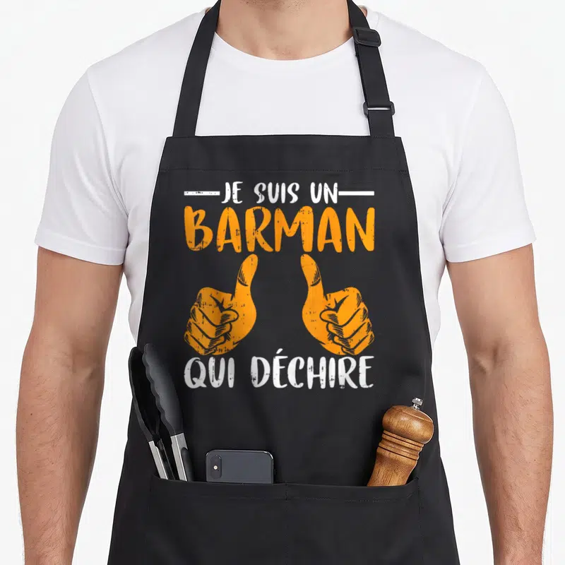 Tablier de cuisine noir avec texte Je Suis Un Barman Qui Déchire et deux mains orange faisant un signe positif.