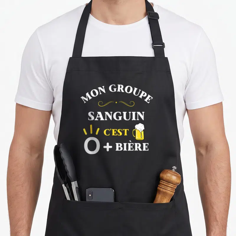 Tablier de cuisine noir avec l'inscription Mon groupe sanguin c'est O plus bière et une illustration de mug de bière jaune.