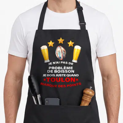Tablier de cuisine noir avec illustration de deux verres de bière, un ballon de rugby et trois étoiles dorées au-dessus du texte imprimé.