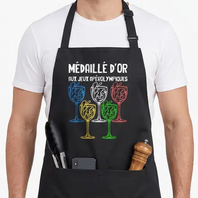 Tablier de cuisine noir avec cinq verres à cocktail colorés et le texte Médaillé d'or aux Jeux Apérolympiques imprimé en blanc.