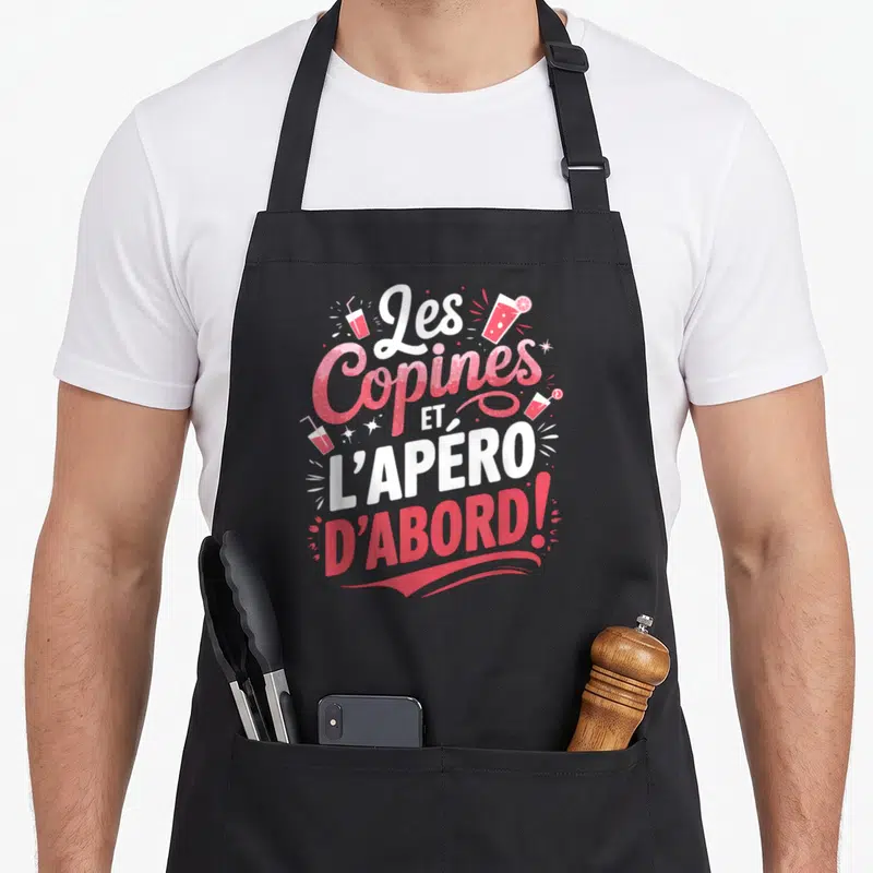 Tablier de cuisine noir avec inscription Les Copines et l'Apéro d'Abord en rose et blanc entouré de verres à cocktail stylisés.