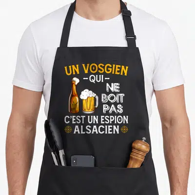 Tablier de cuisine noir avec une bière et le texte Un Vosgien qui ne boit pas c'est un espion alsacien en orange et blanc.