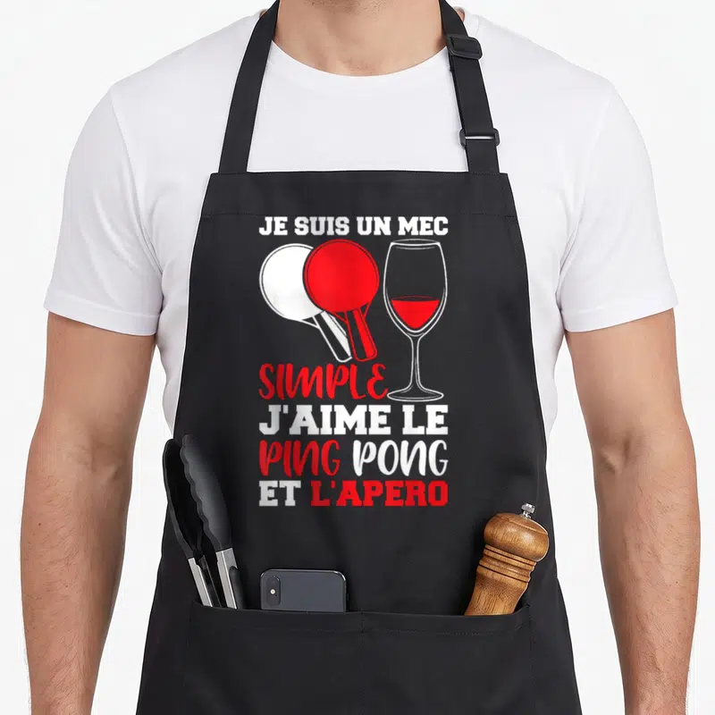 Tablier de cuisine noir avec deux paddles rouge et blanc, un verre de vin rouge et le texte Je suis un mec simple j'aime le ping pong et l'apéro en typographie blanche et rouge.