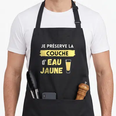 Tablier de cuisine noir avec l'inscription Je préserve la couche d'eau jaune et un verre de pastis.