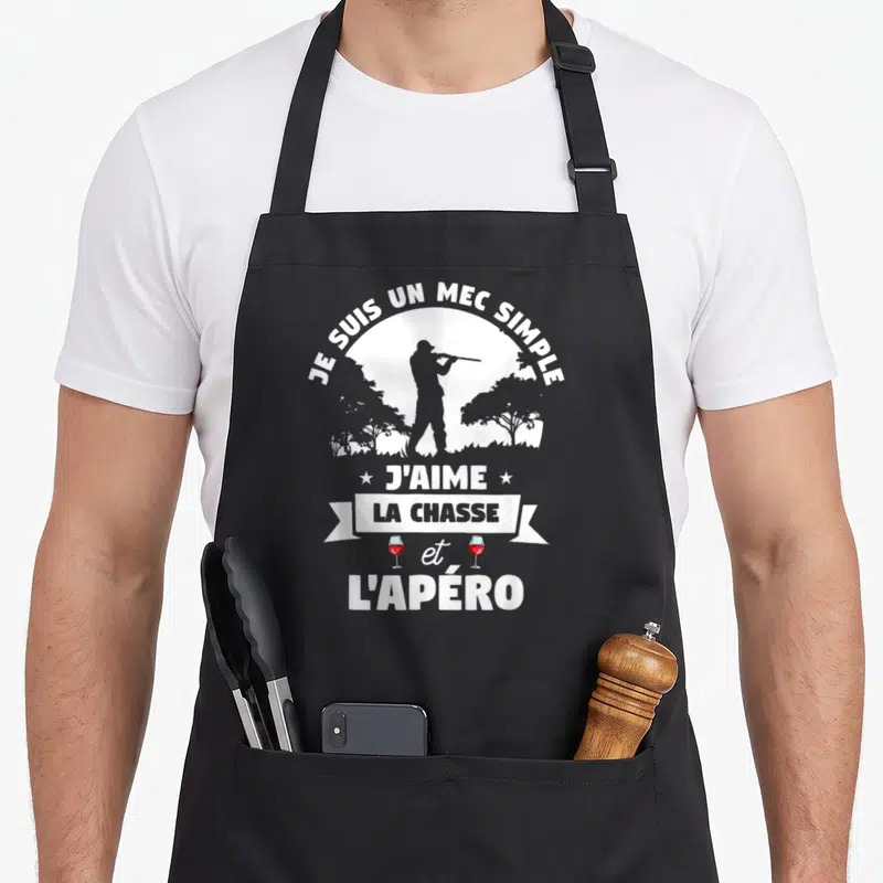 Tablier de cuisine noir avec une silhouette de chasseur, des arbres et le texte Je suis un mec simple j'aime la chasse et l'apéro en blanc.
