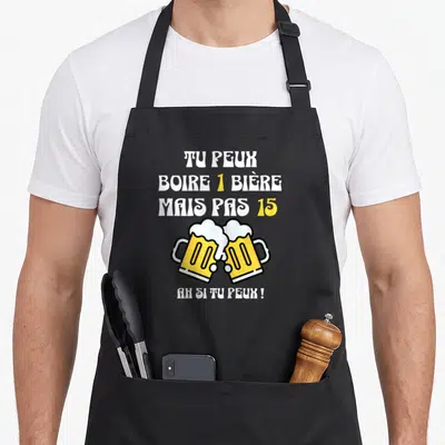 Tablier de cuisine noir avec inscription humoristique sur la bière et deux verres dorés en train de s'entrechoquer.