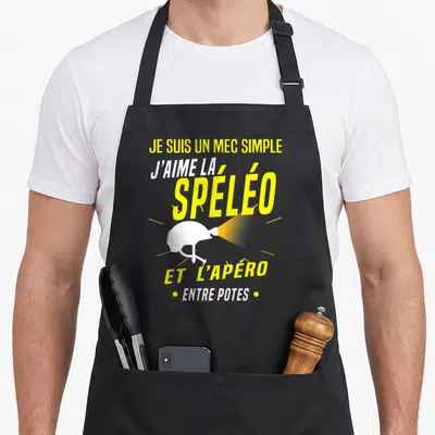 Tablier de cuisine noir avec casque de spéléologie blanc et texte jaune sur fond uni.