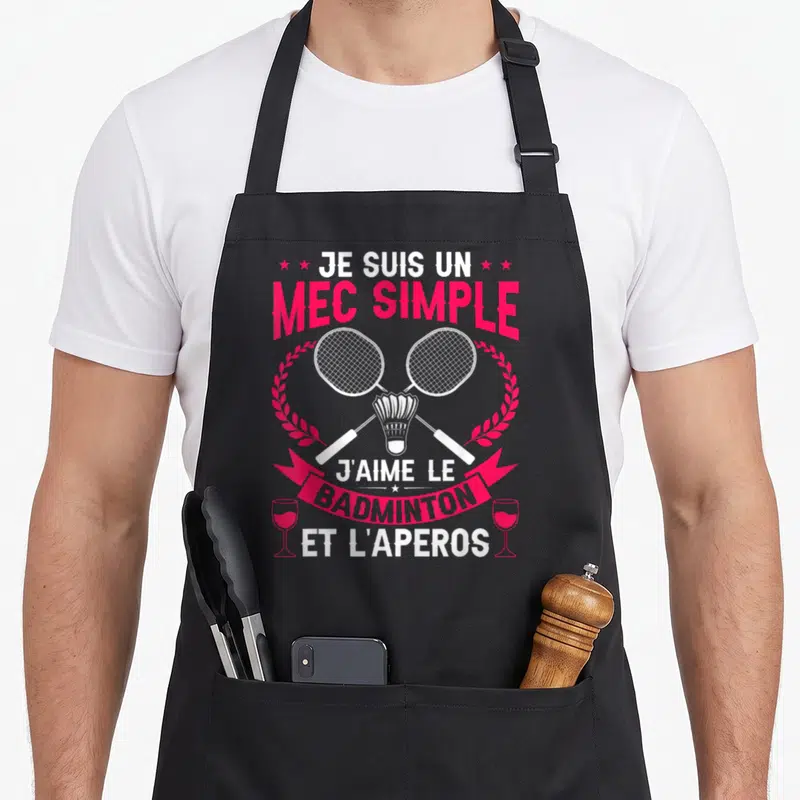 Tablier de cuisine noir avec texte rose et blanc, deux raquettes de badminton croisées et deux verres à vin stylisés.