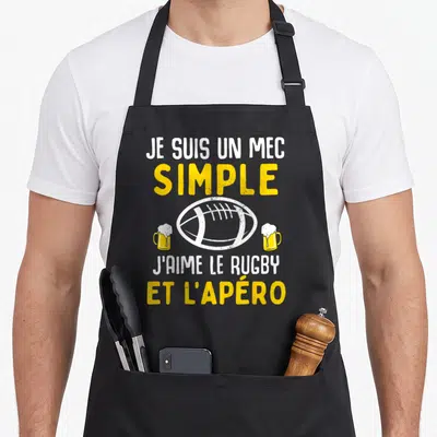 Tablier de cuisine noir avec illustration de ballon de rugby et deux verres de bière sur fond blanc et jaune.
