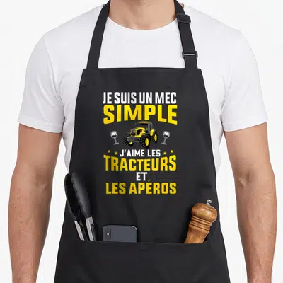 Tablier de cuisine noir avec illustration tracteur jaune et verres à vin sous le texte Je suis un mec simple
