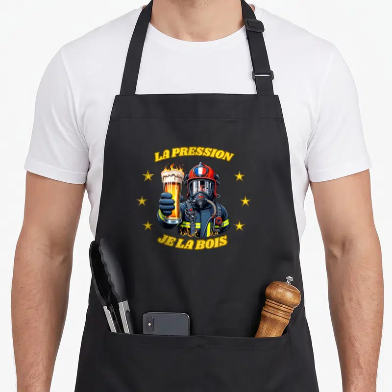 Tablier de cuisine noir avec illustration d'un pompier tenant une bière enflammée et des étoiles dorées.