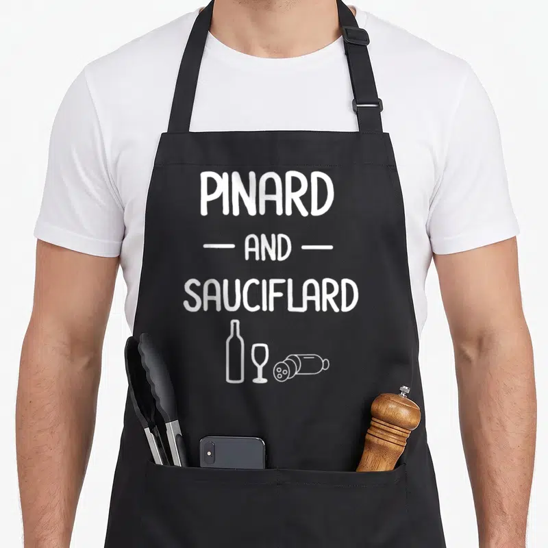 Tablier de cuisine noir avec le texte blanc Pinard and Sauciflard et des dessins de bouteille, verre et saucisson en bas.