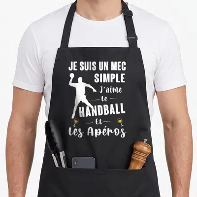Tablier de cuisine noir avec silhouette blanche de handballeur et texte blanc sur fond gris uni.