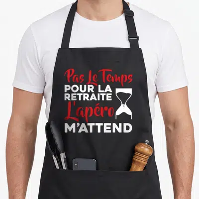 Tablier de cuisine noir avec inscription Pas Le Temps Pour La Retraite L'apéro M'attend et un sablier blanc et rouge.