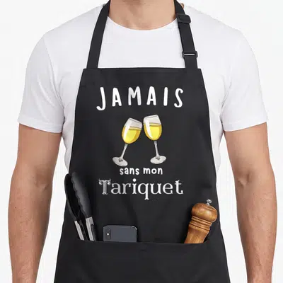 Tablier de cuisine noir avec l'illustration de deux verres de champagne s'entrechoquant et le texte Jamais sans mon Tariquet imprimé en blanc.