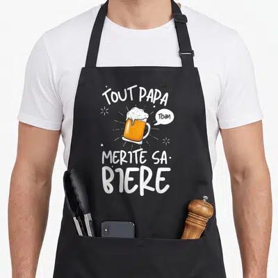Tablier de cuisine noir avec illustration de mug de bière et texte Tout Papa Mérite Sa Bière Tchim en blanc.