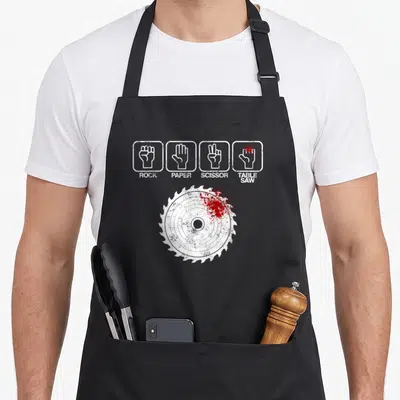 Tablier de cuisine noir avec illustration de main et lame de scie circulaire rouge sanglante