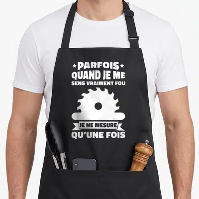 Tablier de cuisine noir avec illustration blanche d'une scie circulaire et texte humoristique sur la mesure unique.