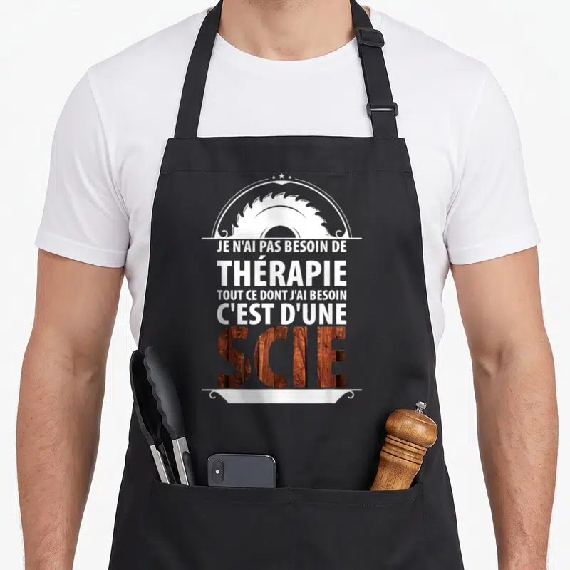 Tablier de cuisine noir avec inscription blanche Je n'ai pas besoin de thérapie et le mot scie en texture bois sous un disque de scie.