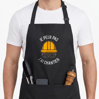Tablier de cuisine noir avec casque de chantier orange et lunettes de protection sous le texte imprimé