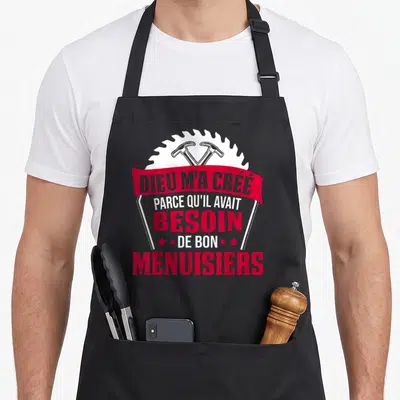 Tablier de cuisine noir avec inscription rouge Dieu m'a créé besoin de bon menuisiers et saw blade blanc en arrière-plan.