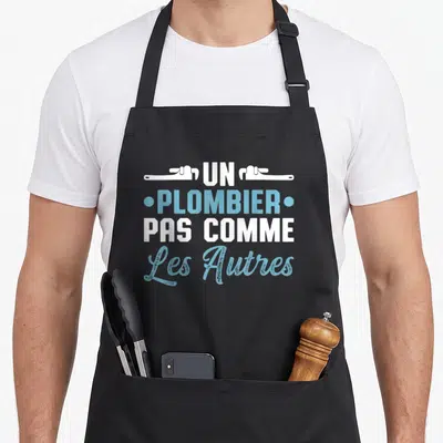 Tablier de cuisine noir avec inscription Un Plombier Pas Comme Les Autres et deux clés anglaises blanches en haut.
