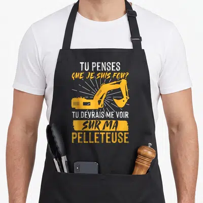 Tablier de cuisine noir avec une illustration de pelleteuse jaune et un message humoristique en blanc et orange sur le devant.