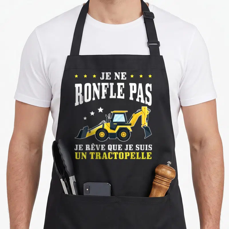Tablier de cuisine noir avec une illustration de tractopelle jaune et le texte Je ne ronfle pas je rêve que je suis un tractopelle