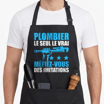 Tablier de cuisine noir avec une main tenant une clé à molette et le texte Plombier le seul le vrai en bleu et blanc.