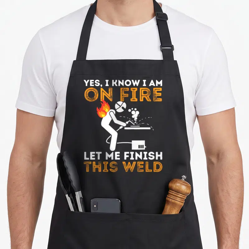 Tablier de cuisine noir avec une illustration de soudeur en feu et texte Yes I know I am on fire let me finish this weld.